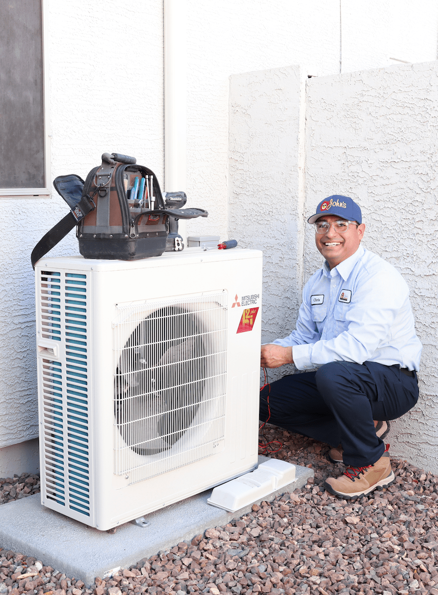 A smiling John’s technician working on a heat pump in Gilbert